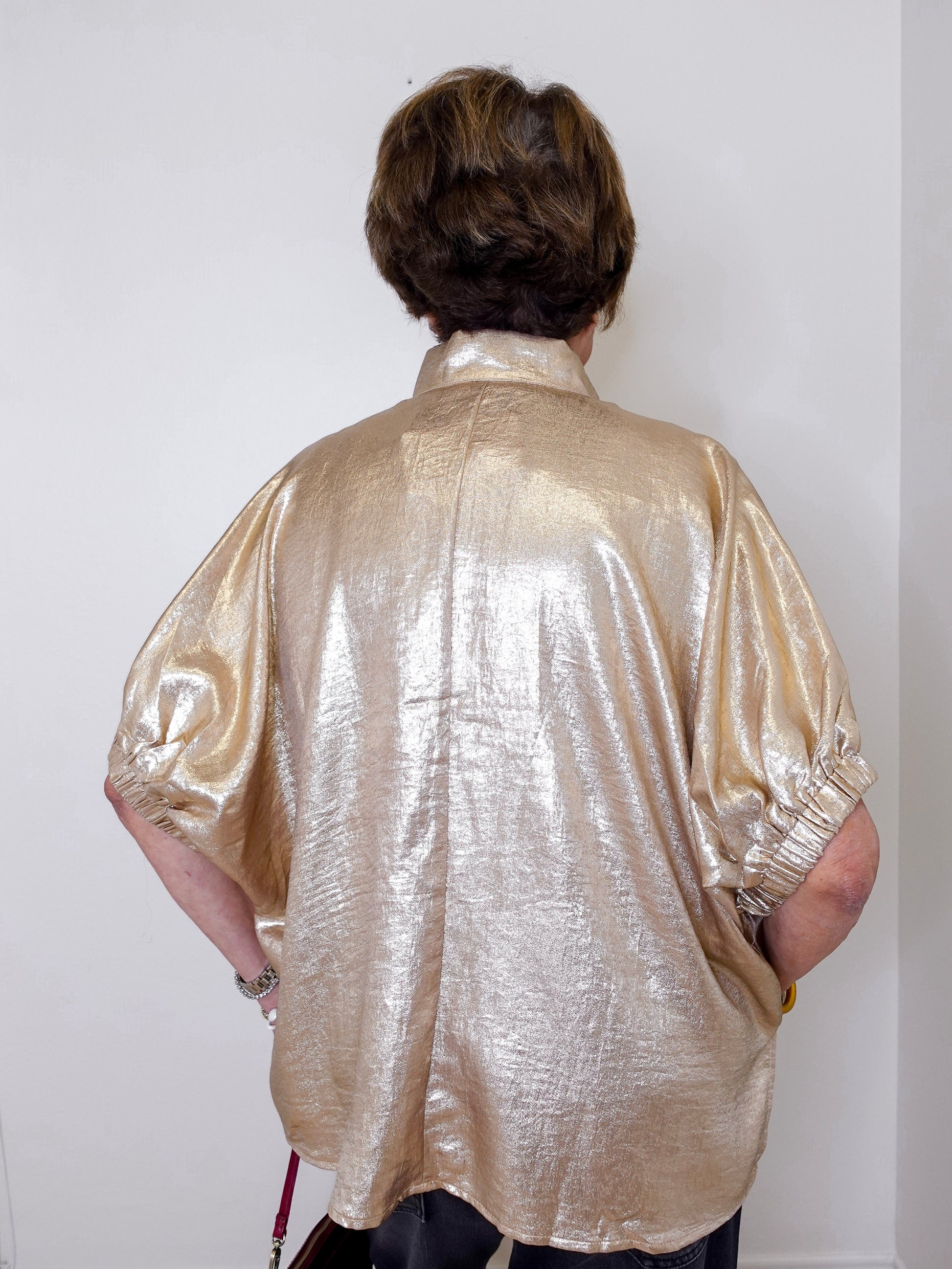 Person wearing a shiny gold shirt against a white wall