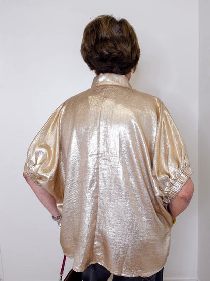 Person wearing a shiny gold shirt against a white wall