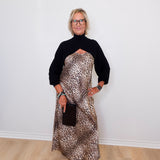 Person wearing a black turtleneck and leopard print dress against a white wall.
