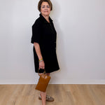 Woman in a black dress holding a brown bag against a white wall.