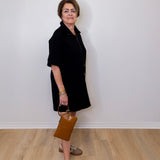 Woman in a black dress holding a brown bag against a white wall.