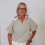 Woman wearing a striped shirt and white pants against a plain background