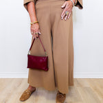 Person wearing a brown outfit with a maroon handbag on a light wooden floor.