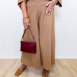 Person wearing a brown outfit with a maroon handbag on a light wooden floor.