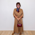 Woman in a beige dress with a red handbag against a white wall