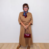 Woman in a beige dress with a red handbag against a white wall