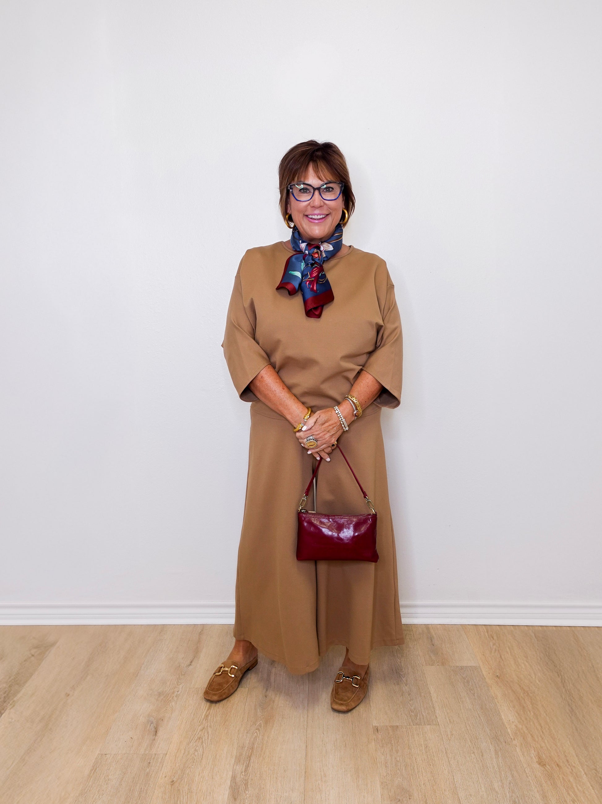Woman in a beige dress with a red handbag against a white wall