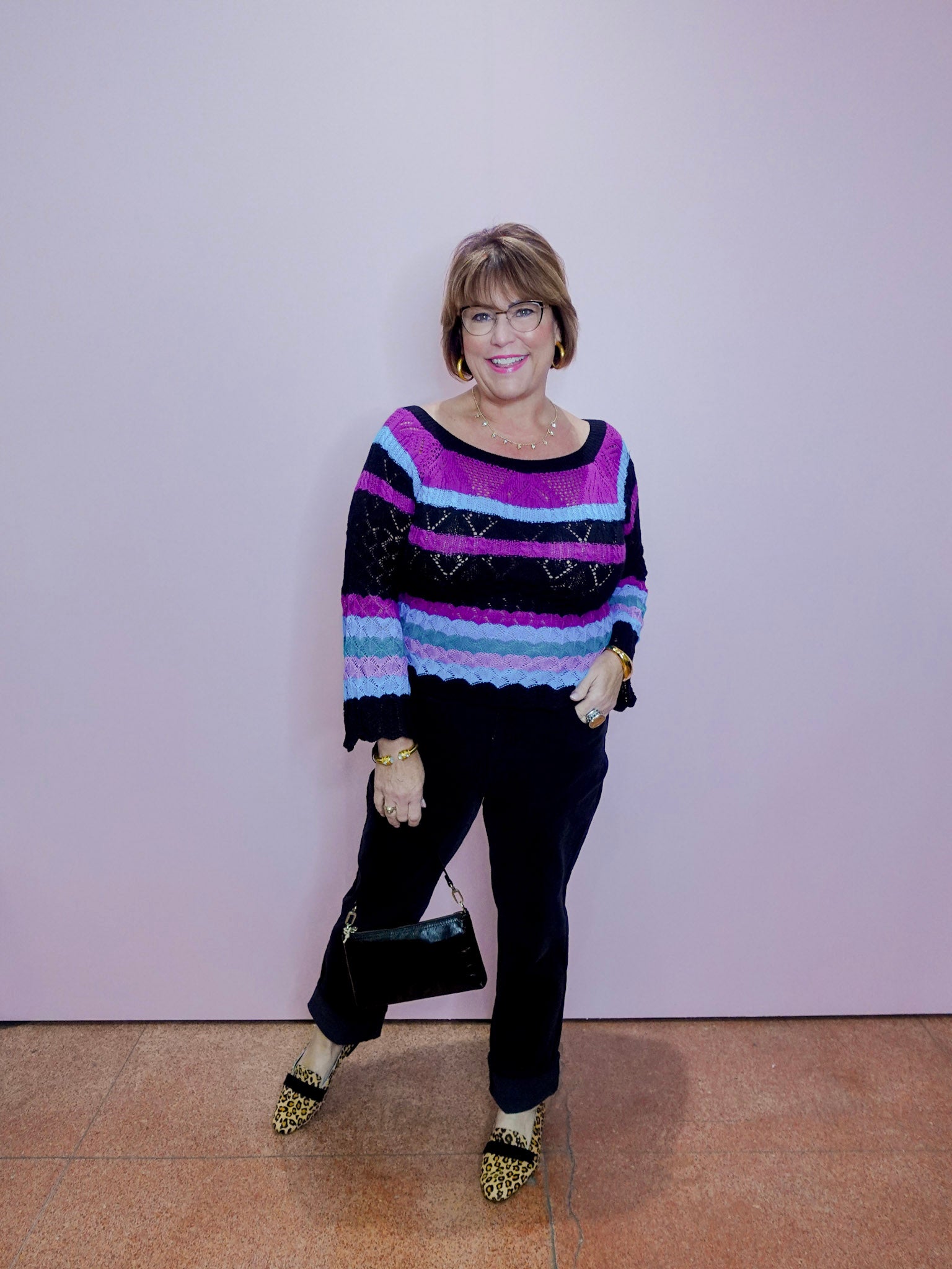 Woman wearing a colorful sweater and black pants against a plain background