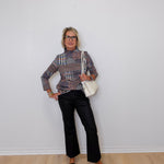Person wearing a patterned blouse, black pants, and black shoes against a white wall.