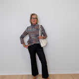 Person wearing a patterned blouse, black pants, and black shoes against a white wall.