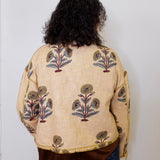 Person wearing a beige embroidered jacket with floral patterns on a plain background