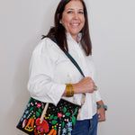 Woman holding a black handbag with colorful floral embroidery against a plain background