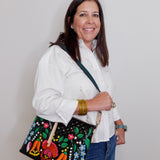 Woman holding a black handbag with colorful floral embroidery against a plain background
