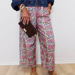 Person wearing a denim jacket, patterned pants, and brown loafers against a white wall.