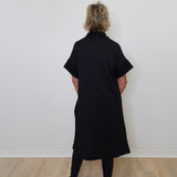 Person wearing a black dress standing against a white wall.