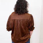 Person wearing a brown blouse with puffed sleeves against a white background