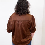 Person wearing a brown blouse with puffed sleeves against a white background