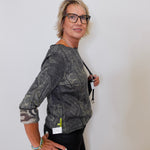 Woman wearing a patterned gray top and black pants against a plain background