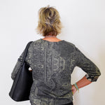 Person wearing a patterned shirt holding a black bag against a white background