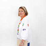 Woman wearing a white blouse with floral embroidery and blue pants against a white background