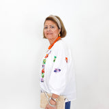 Woman wearing a white blouse with floral embroidery and blue pants against a white background