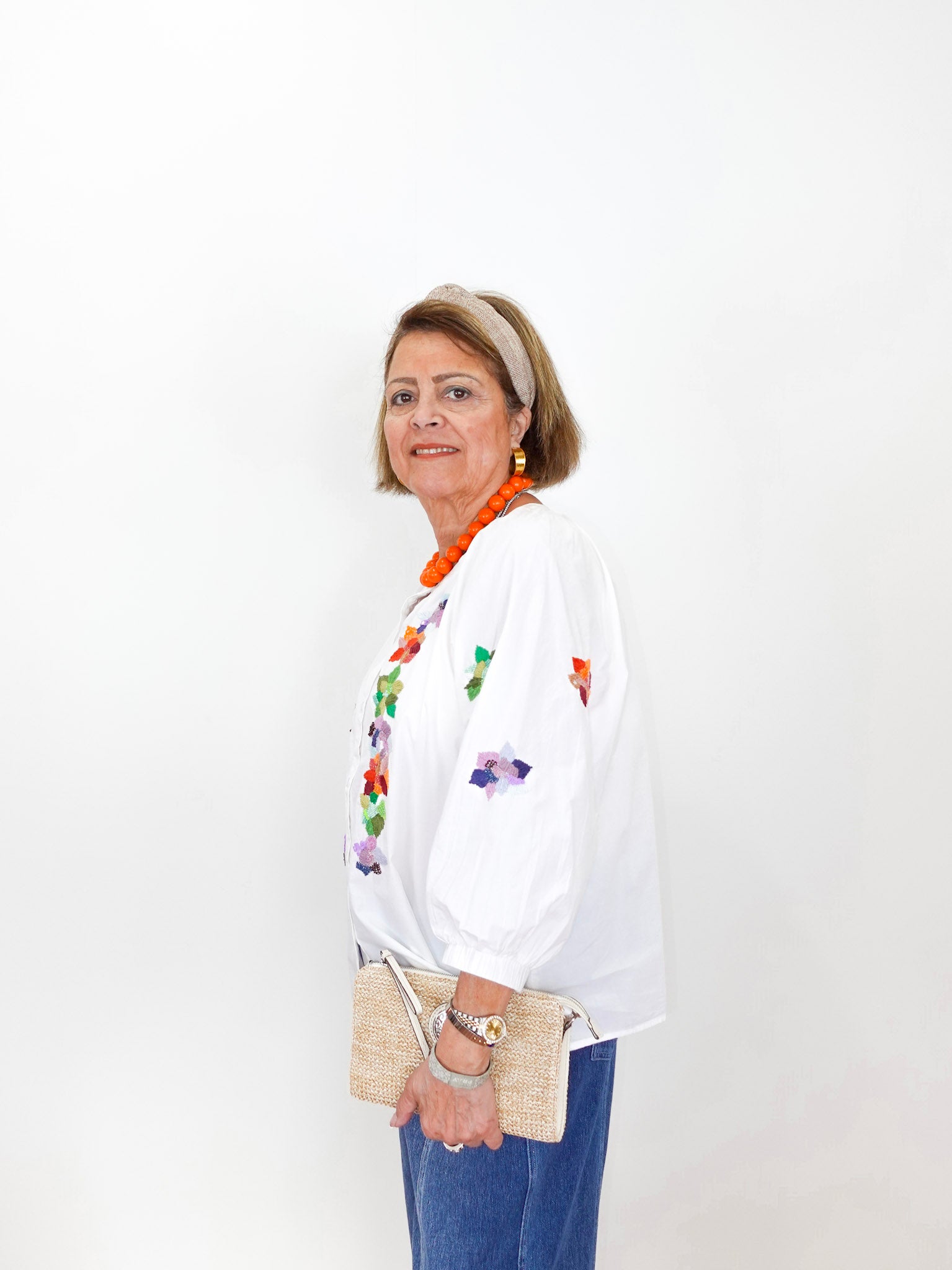 Woman wearing a white blouse with floral embroidery and blue pants against a white background