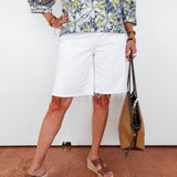 Person wearing a floral shirt, white shorts, and brown sandals on a plain background