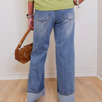 Person wearing blue jeans and a green top, holding a brown handbag indoors.