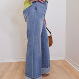 Person wearing blue jeans and a green top, standing on a wooden floor with a white wall background.