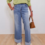 Person wearing a green shirt and blue jeans holding a brown handbag indoors.