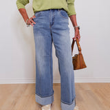 Person wearing a green shirt and blue jeans holding a brown handbag indoors.