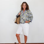 Woman wearing a floral blouse and white shorts, holding a bag against a white background