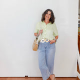 Woman wearing a light green shirt and blue jeans standing against a white wall.