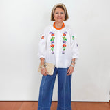 Woman wearing a white blouse with floral embroidery and blue jeans on a white background