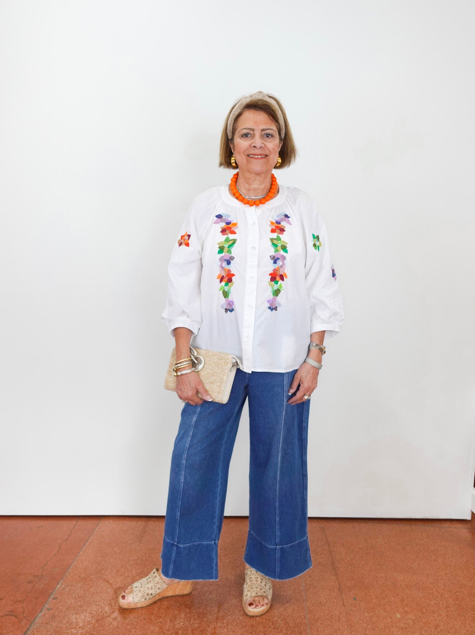 Woman wearing a white blouse with floral embroidery and blue jeans on a white background