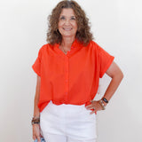 Woman wearing an orange blouse and white pants against a plain background