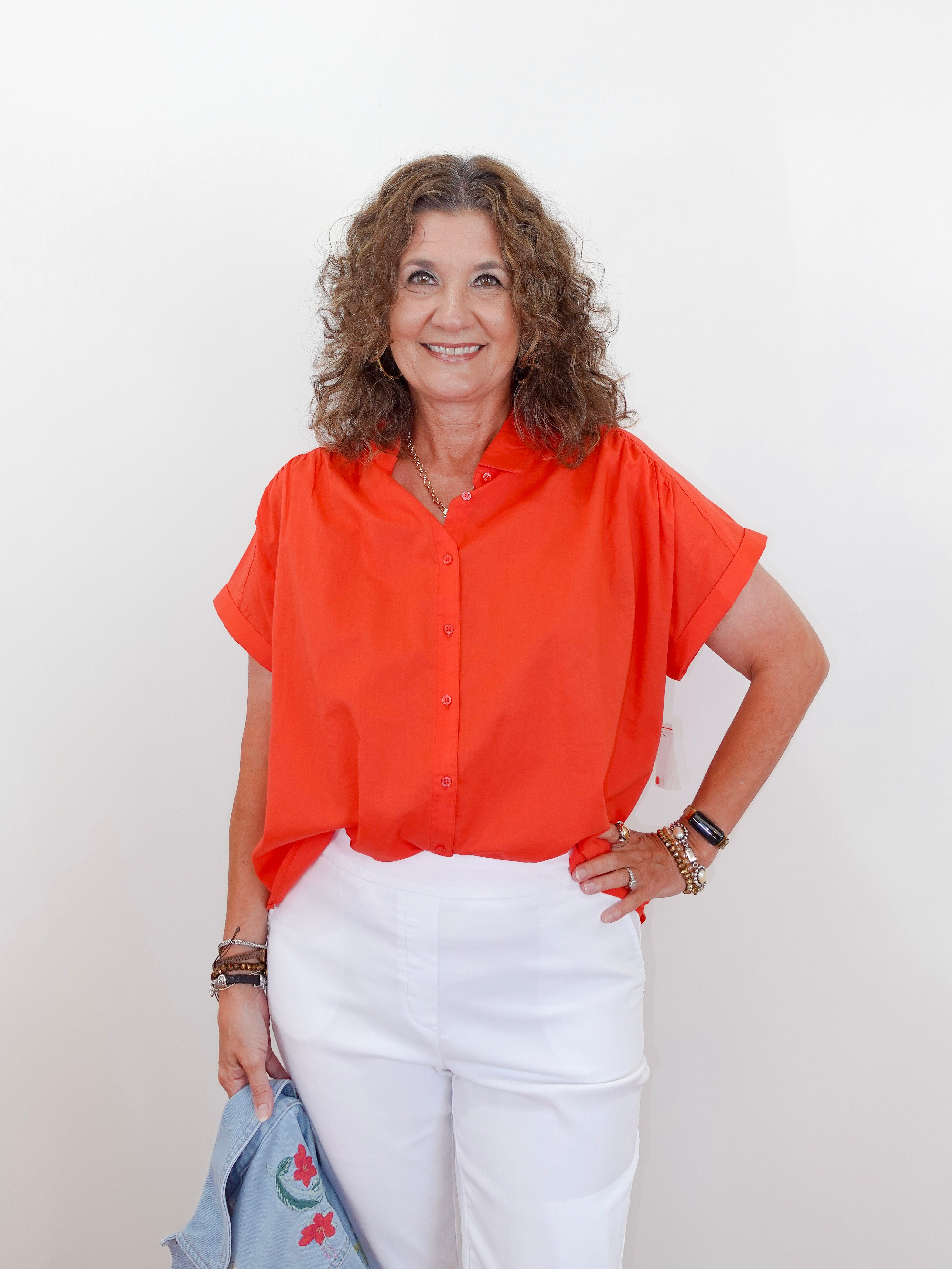 Woman wearing an orange blouse and white pants against a plain background