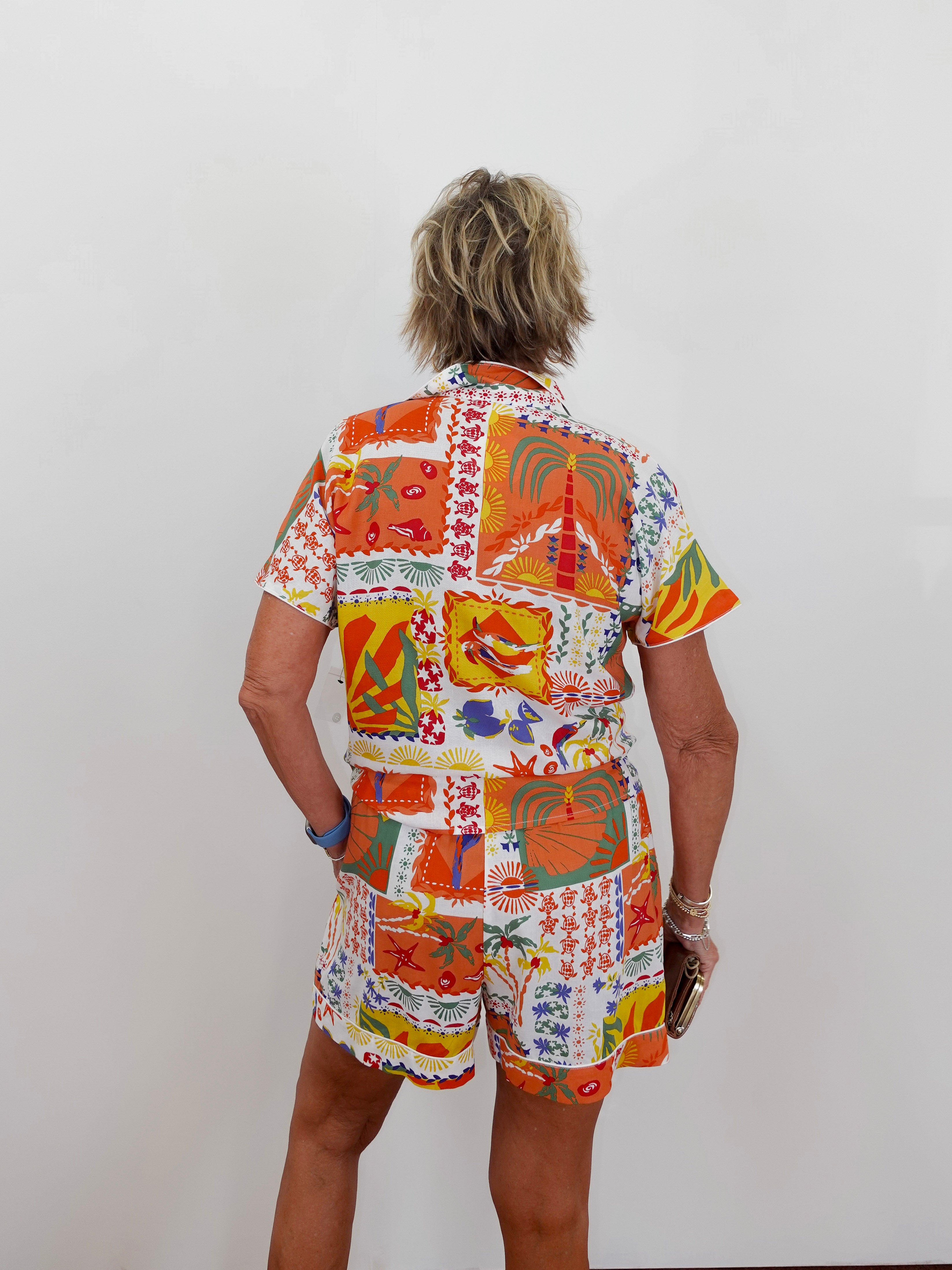Person wearing a colorful patterned shirt and shorts set on a plain background