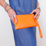 Person holding an orange clutch bag with a plain background
