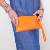 Person holding an orange clutch bag with a plain background