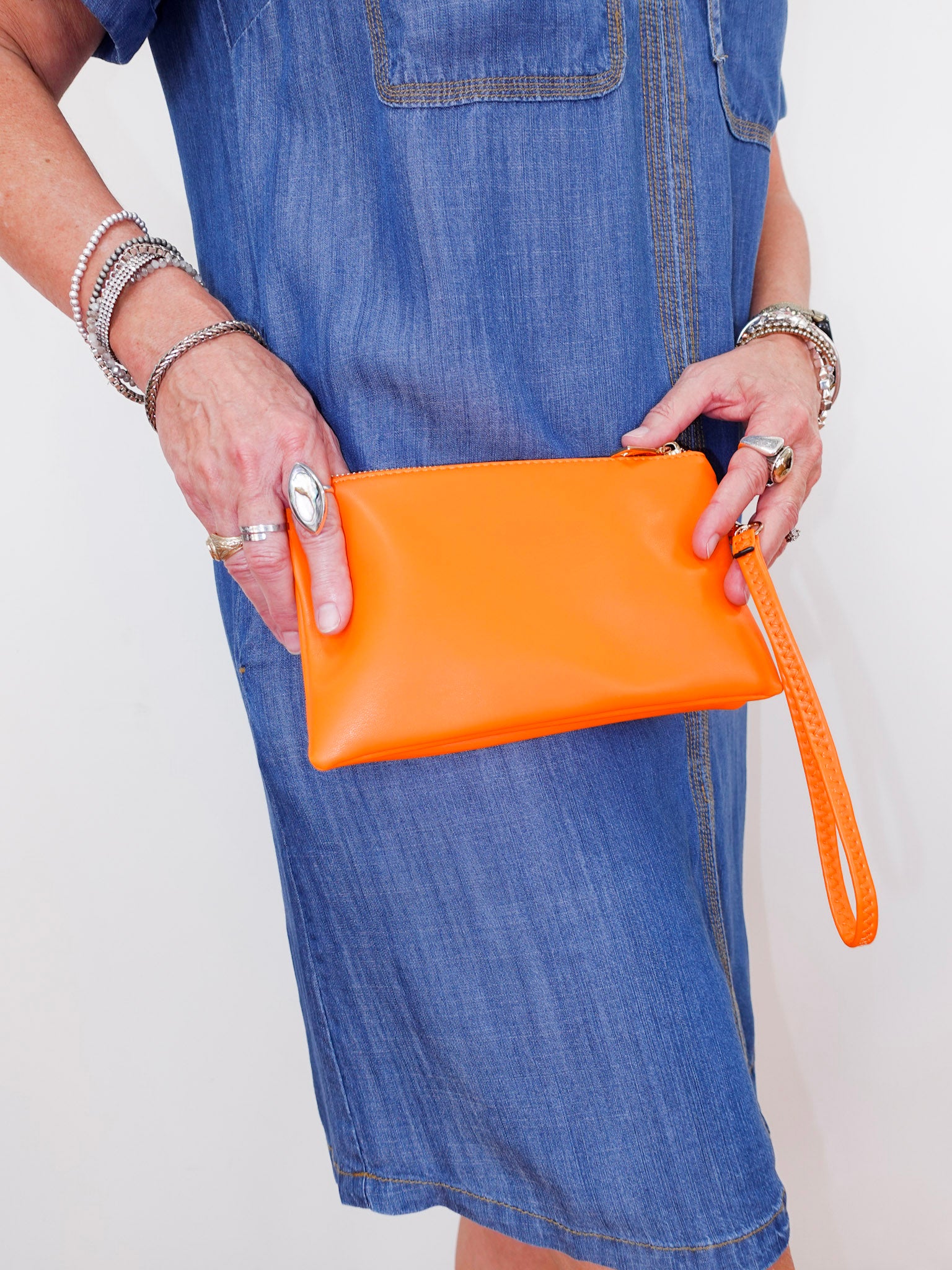 Person holding an orange clutch bag with a plain background