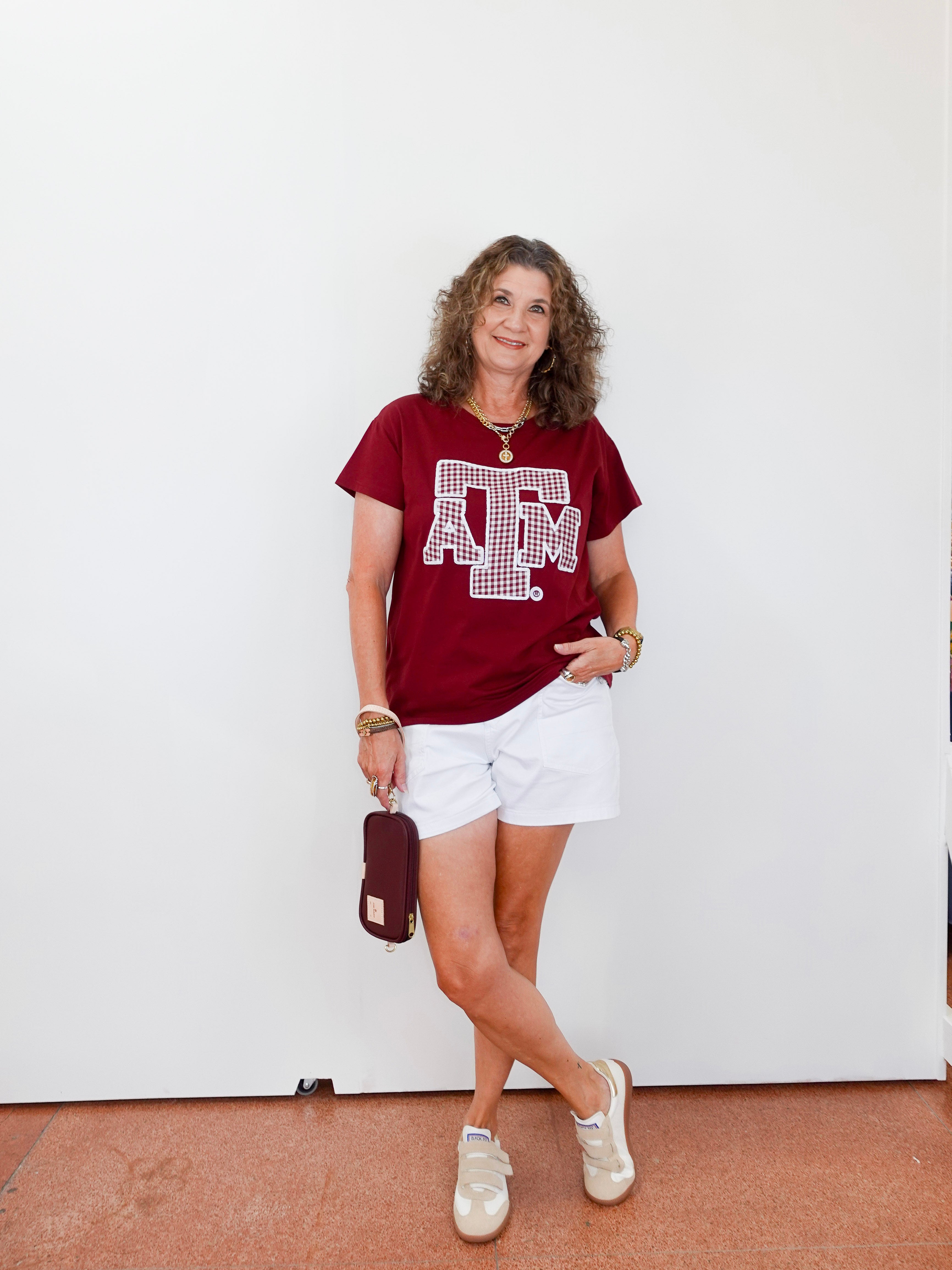 Woman wearing a red t-shirt with a logo and white shorts, standing against a white wall.