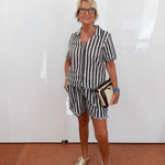 Woman wearing a black and white striped outfit with beige shoes against a white wall.