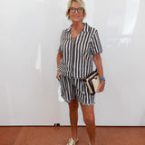 Woman wearing a black and white striped outfit with beige shoes against a white wall.
