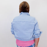 Person wearing a light blue denim jacket over a pink top and blue floral pants on a white background