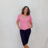 Woman wearing a pink and white striped shirt with navy pants against a plain background