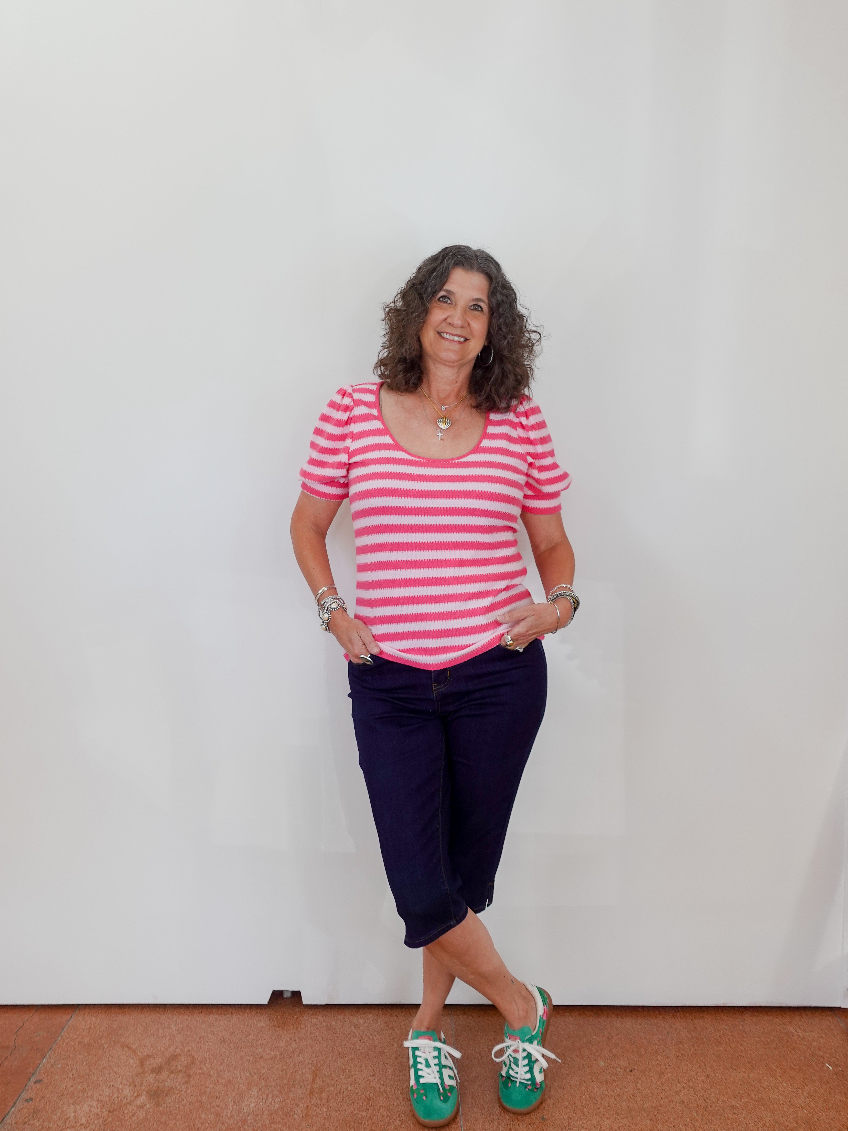 Woman wearing a pink and white striped shirt with navy pants against a plain background