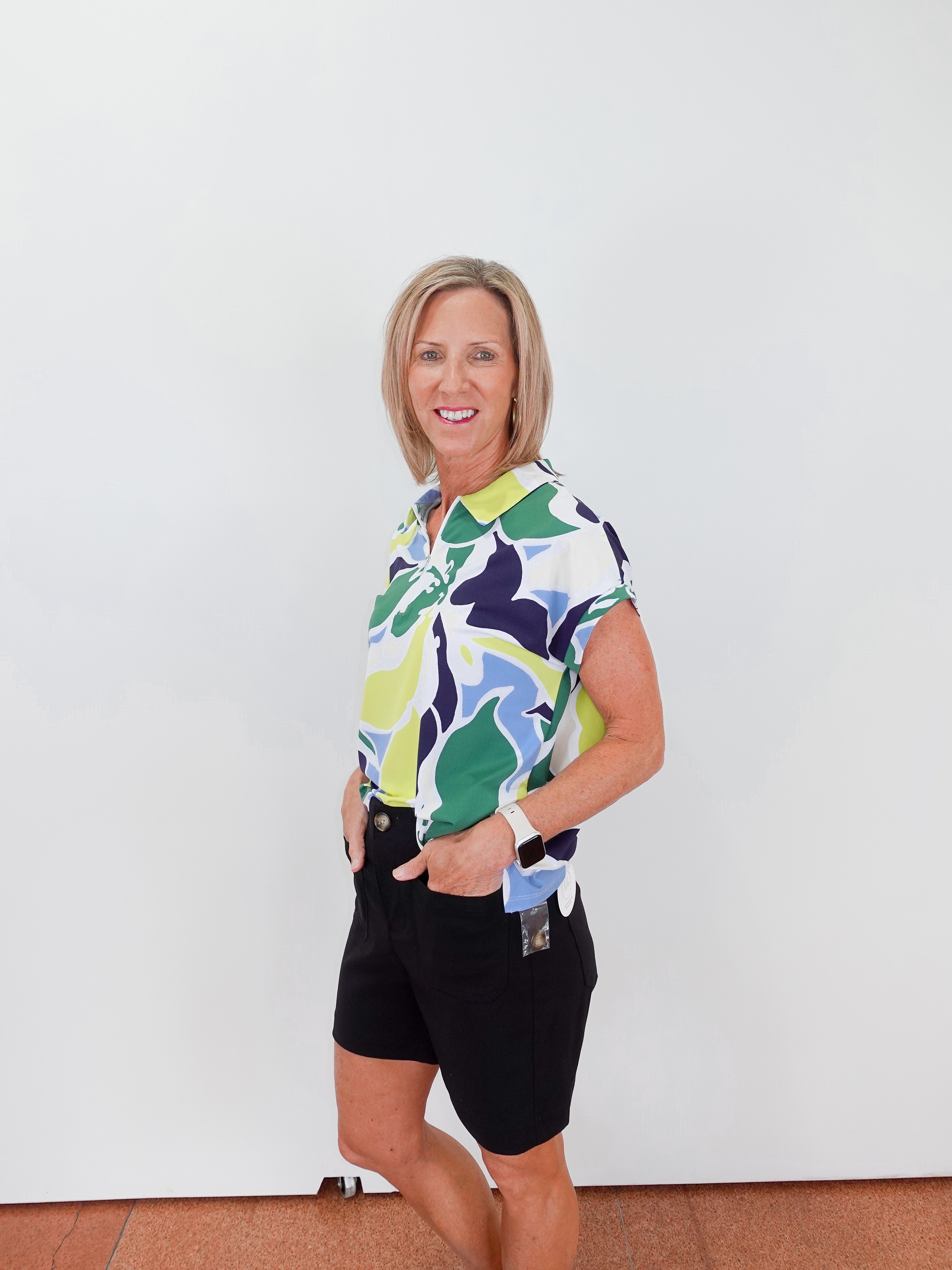 Woman wearing a colorful patterned shirt and black shorts against a white background