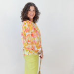 Woman wearing a colorful floral blouse and bright yellow pants against a white background