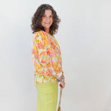 Woman wearing a colorful floral blouse and bright yellow pants against a white background